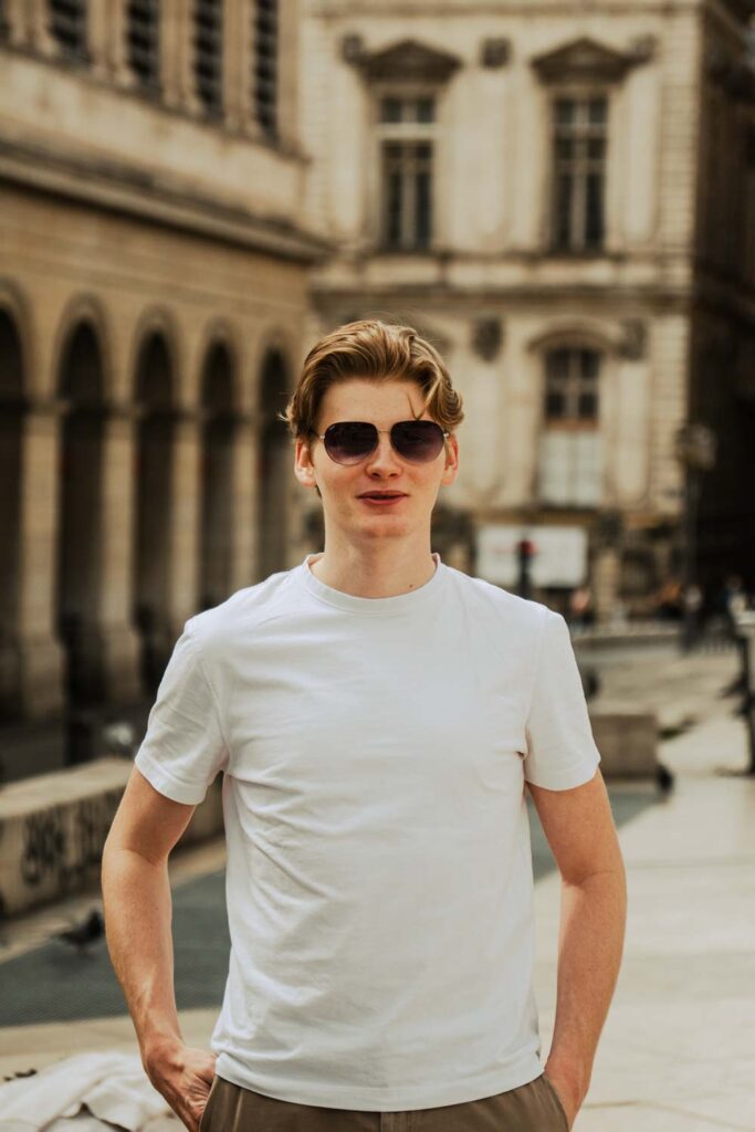 Un jeune homme portant des lunettes de soleil se tient droit et sourit pour la photo.